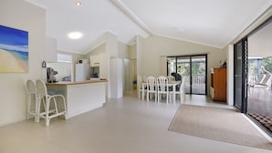 Amplia sala de estar con cocina, mesa de comedor y puerta corrediza de vidrio que da a una terraza exterior.