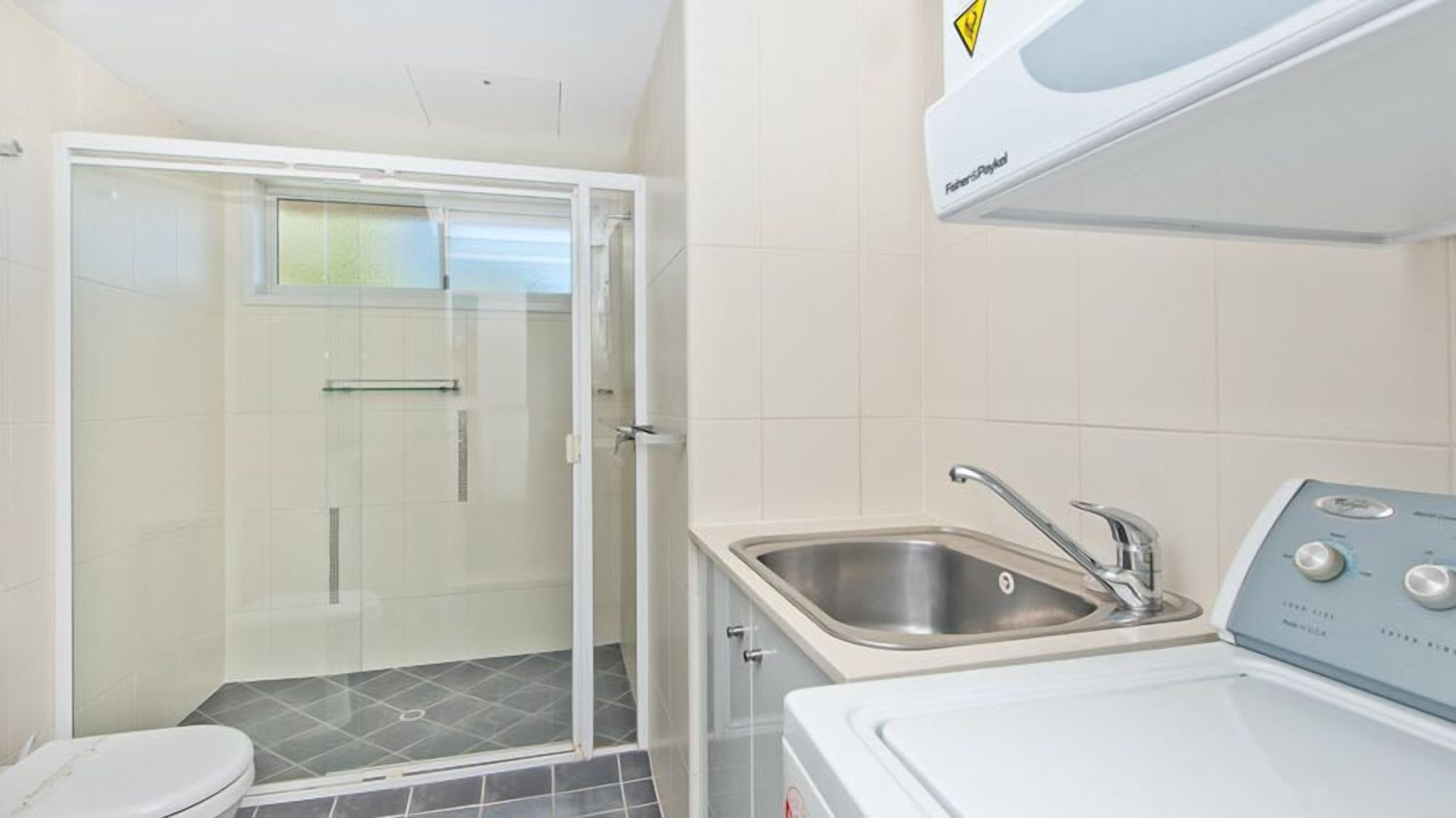 A bathroom with a glass shower enclosure, a sink, and a washing machine.