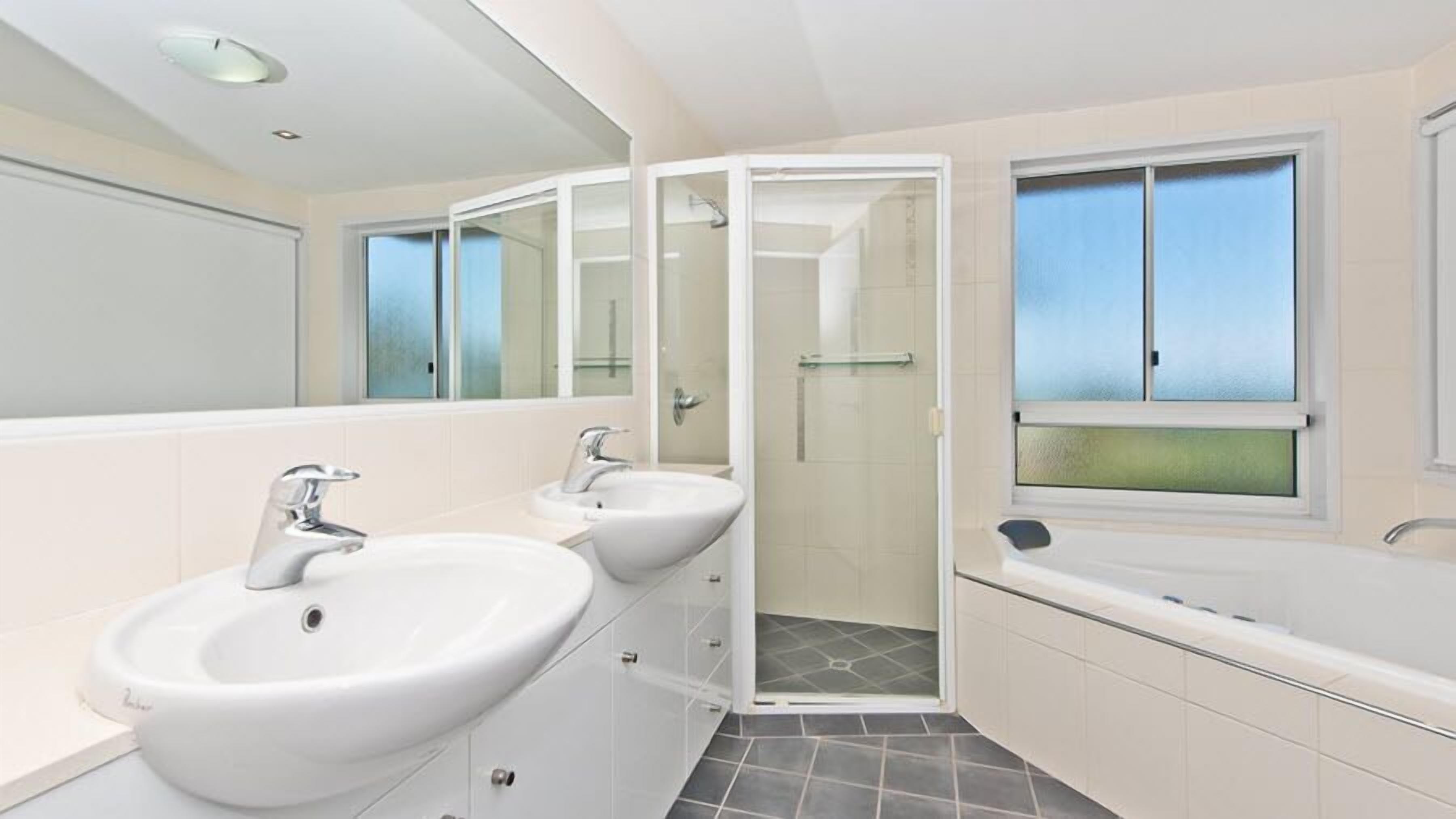 A modern bathroom with two sinks, a shower enclosure, and a bathtub.