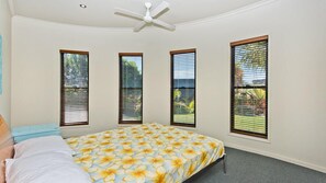 Un dormitorio con cama, ventilador de techo y tres ventanas con persianas.