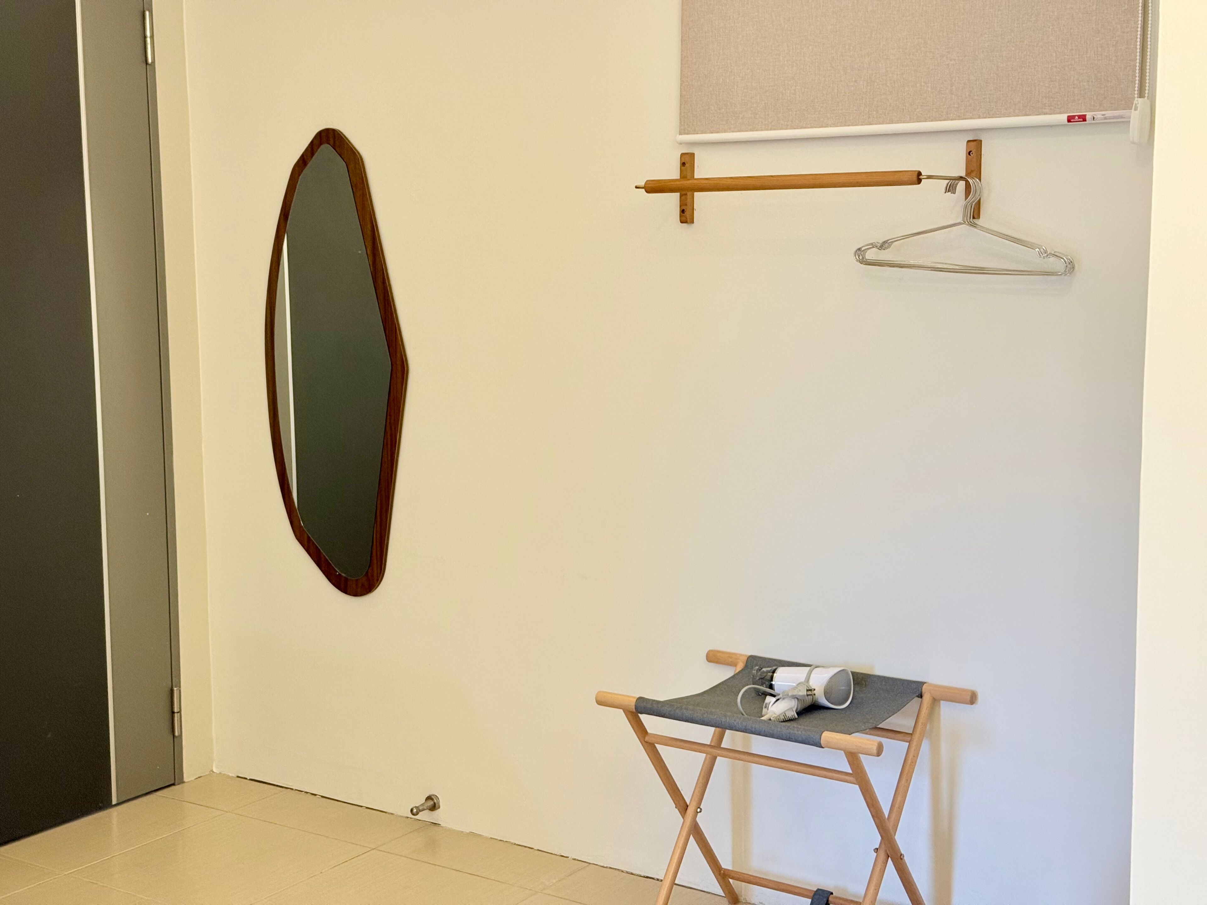 A room with a wooden door, a mirror, a small folding table with a cup, and a clothes hanger.