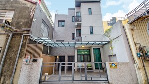 Ein modernes Gebäude mit geschlossenem Eingangsbereich, einer kleinen Außenbereich-Sitzgelegenheit und einem sichtbaren Balkon.