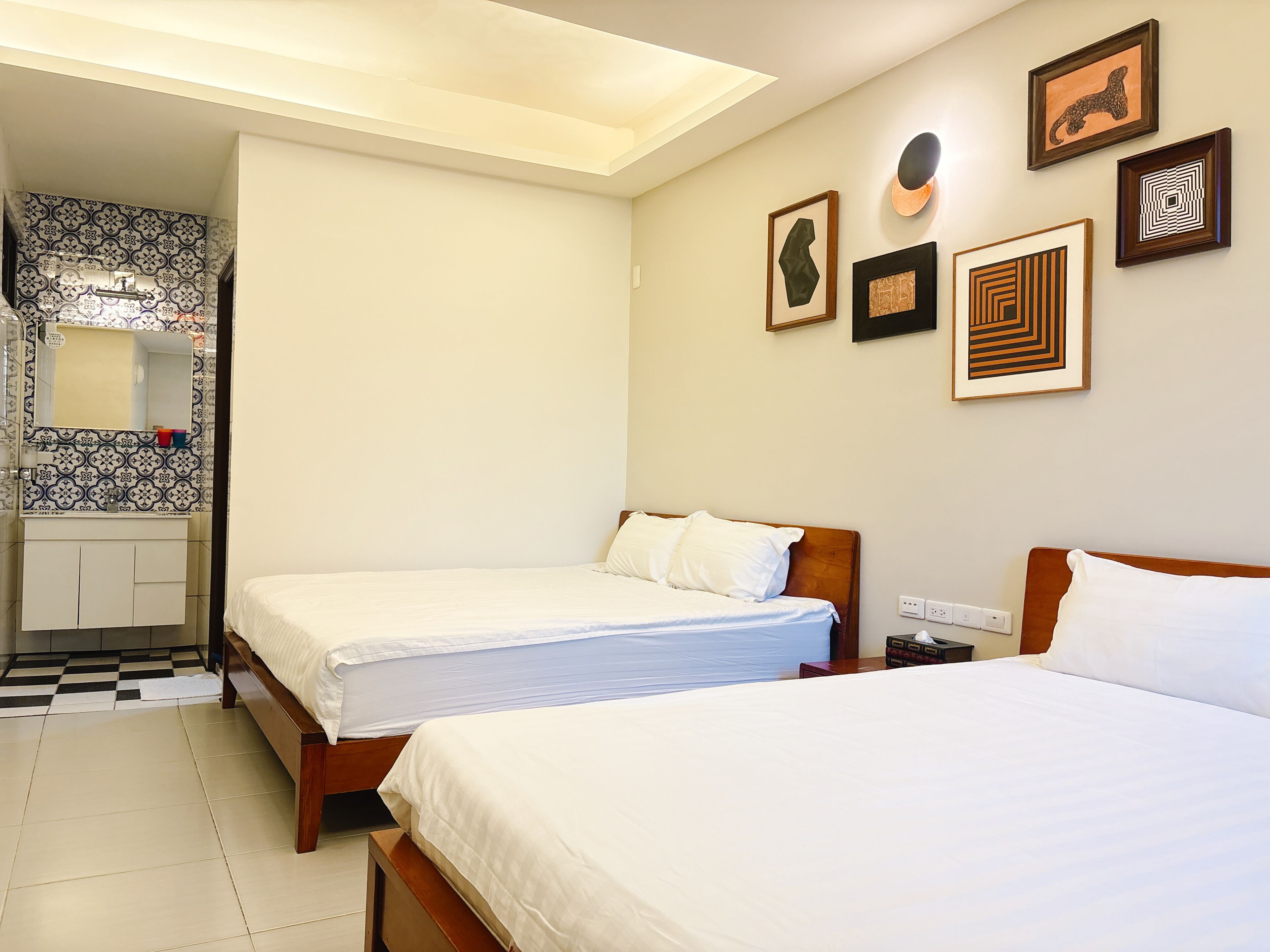 A hotel room with two beds, a bathroom with patterned tiles, and wall art.