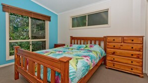 Ein Schlafzimmer mit einem hölzernen Bett, einem Schminktisch, einem Fenster und Blick auf Grünfläche.