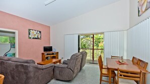 Ein Wohnzimmer mit einem Ecksofa, einem Holztisch, einer TV-Konsole und einem Esstisch mit Stühlen.