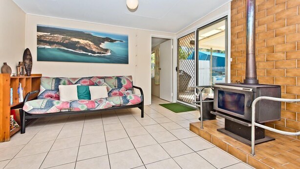 A living room with a sofa, a painting of a coastal landscape, a fireplace, and a door leading to another room. - Curlew Corner (Cowan Cowan)
