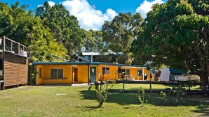 A yellow building with a covered patio area, surrounded by trees and a grassy yard. - Curlew Corner (Cowan Cowan)