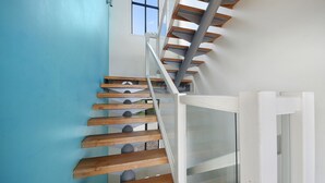 Un escalier moderne avec des marches en bois et des rampes en verre, menant à un palier situé au deuxième étage.