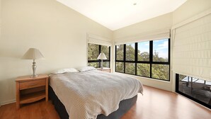 Une chambre avec un grand lit, deux tables de chevet, une fenêtre avec des stores et une vue sur les arbres.