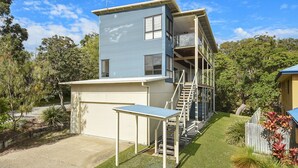 Un bâtiment à deux étages, à la façade bleue, doté d’un espace extérieur couvert avec une table et des chaises, et d’un escalier menant à un niveau supérieur.