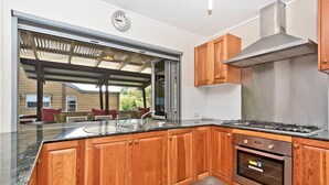A modern kitchen with wooden cabinets, a stainless steel range hood, and a built-in oven. - Moreton Magic (Cowan Cowan)