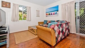A cozy living room with a wicker sofa, a TV, and a view of the outdoors through a sliding door. - Moreton Magic (Cowan Cowan)