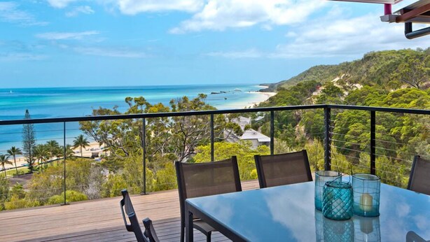 Un balcon avec une table et des chaises donnant sur une plage et l’océan.