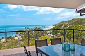A balcony with a table and chairs overlooking a beach and ocean.