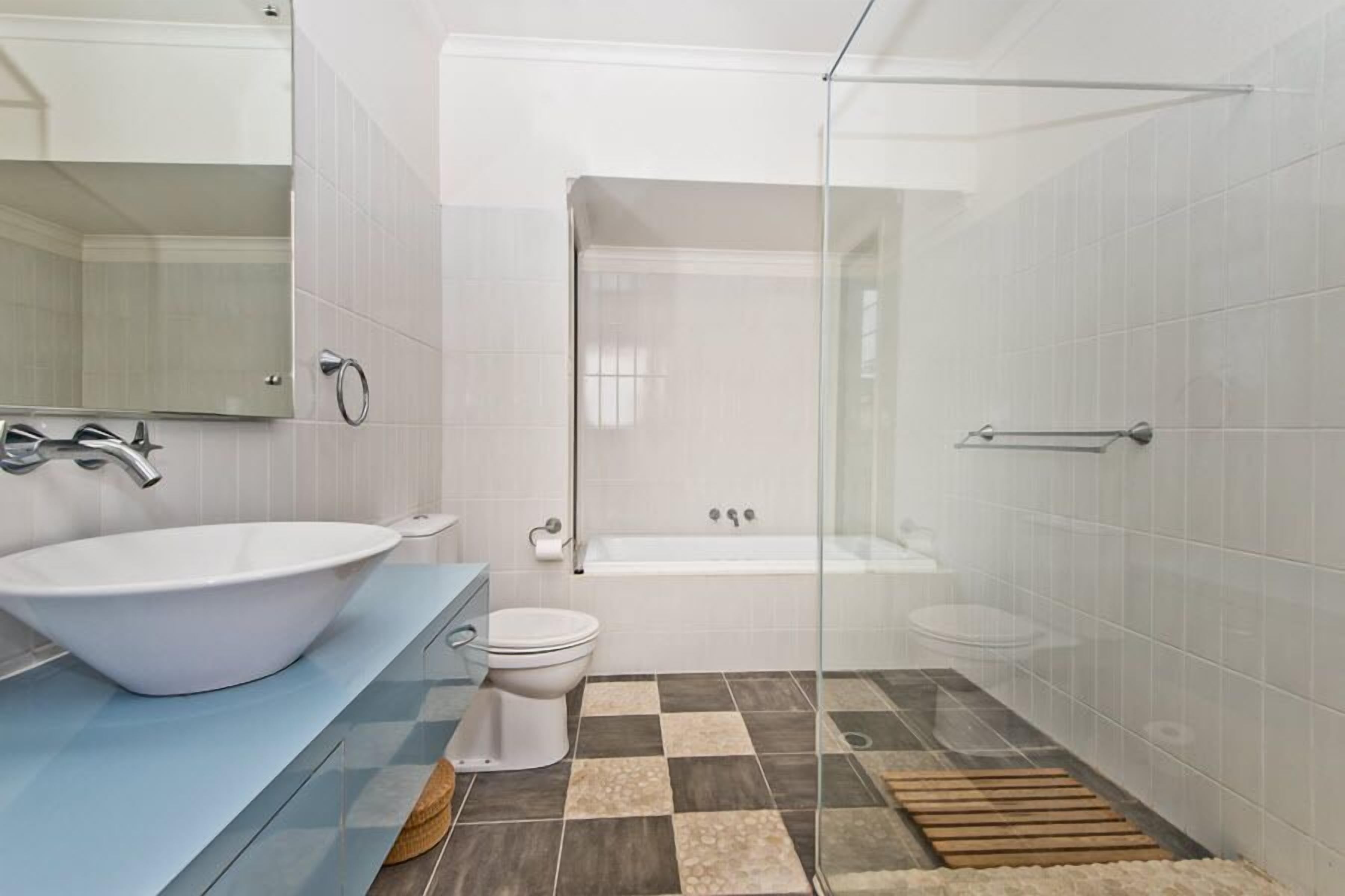 Un baño moderno con un lavamanos grande de color blanco, una ducha con cerramiento de vidrio y un inodoro.