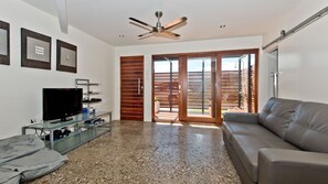 A living room with a TV, glass coffee table, leather sofa, and a sliding glass door leading to an outdoor area.