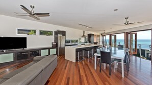 A modern kitchen with a central island, a dining area with a large table and chairs, a gray sofa, and a TV on a cabinet.