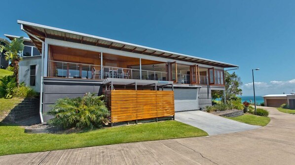 A modern two-story house with a large balcony, a garage, and a well-maintained lawn.