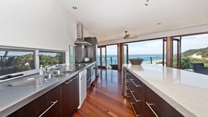 A modern kitchen with a large island, stainless steel appliances, and a view of the ocean.