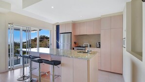 A modern kitchen with a large island, bar stools, a stainless steel refrigerator, and a view through the glass doors. - Tangalooma Moreton Getaway (Moreton Island)