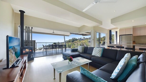 A modern living room with a large sofa, a glass coffee table, and a fireplace. There is a balcony with a view of the ocean. - Tangalooma Moreton Getaway (Moreton Island)