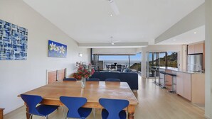 A modern dining area with a wooden table and blue chairs, a sofa, and a view of the ocean. - Tangalooma Moreton Getaway (Moreton Island)
