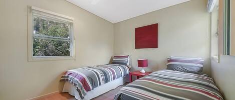 A bedroom with two beds, a window, a ceiling fan, and a red wall decoration.