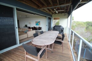 An outdoor deck with a wooden table and chairs, a barbecue grill, and a sliding glass door leading to an interior living area with a sofa and chairs. - Tangalooma Panoramic (Moreton Island)
