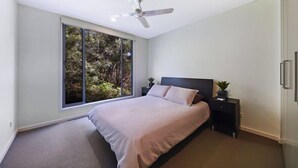 Un dormitorio moderno con un ventanal grande, una cama, una mesita de noche y un ventilador de techo.