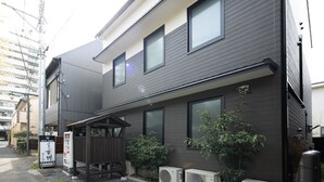 Un edificio moderno de dos pisos con fachada oscura, varias ventanas y una pequeña zona cubierta con plantas.