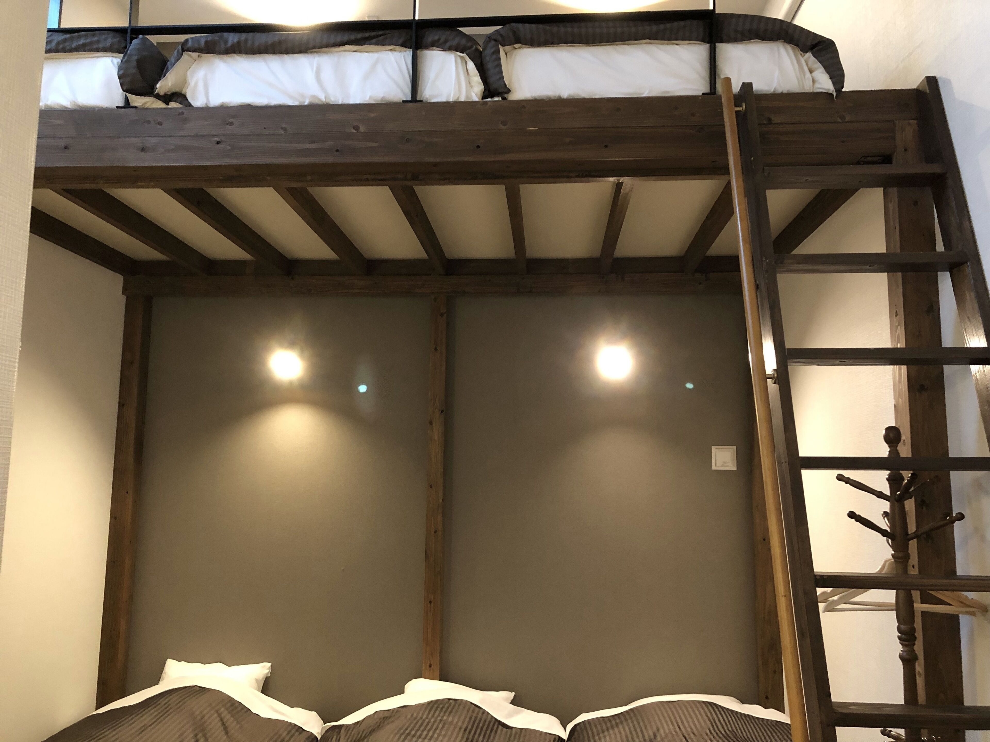 Un lit superposé avec une échelle en bois, deux tables de chevet et un porte-manteau fixé au mur.