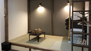 Una habitación con suelo de estera de tatami, una mesita con toallas dobladas, una escalera de madera y una cama con cabecero.