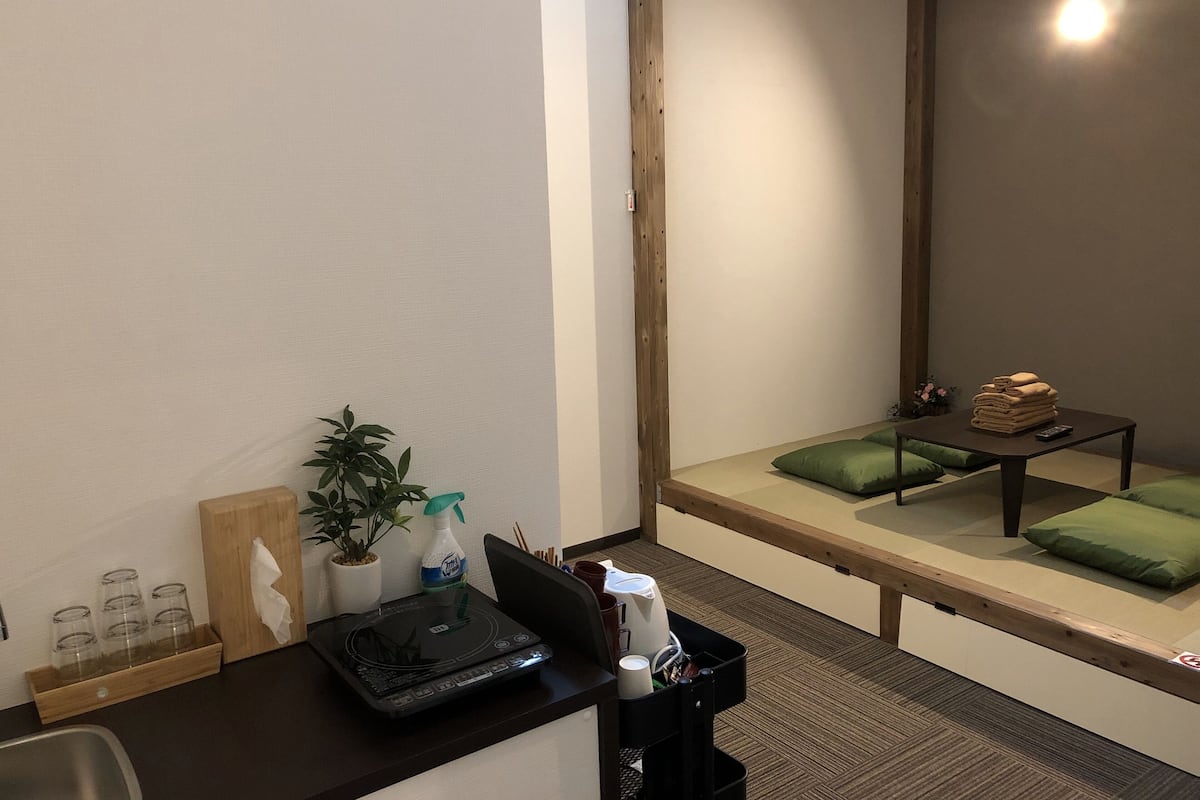 Ein Zimmer mit einem Bett, einem kleinen Tisch mit Handtüchern, einer Pflanze und einem Laptop auf einem Schreibtisch.