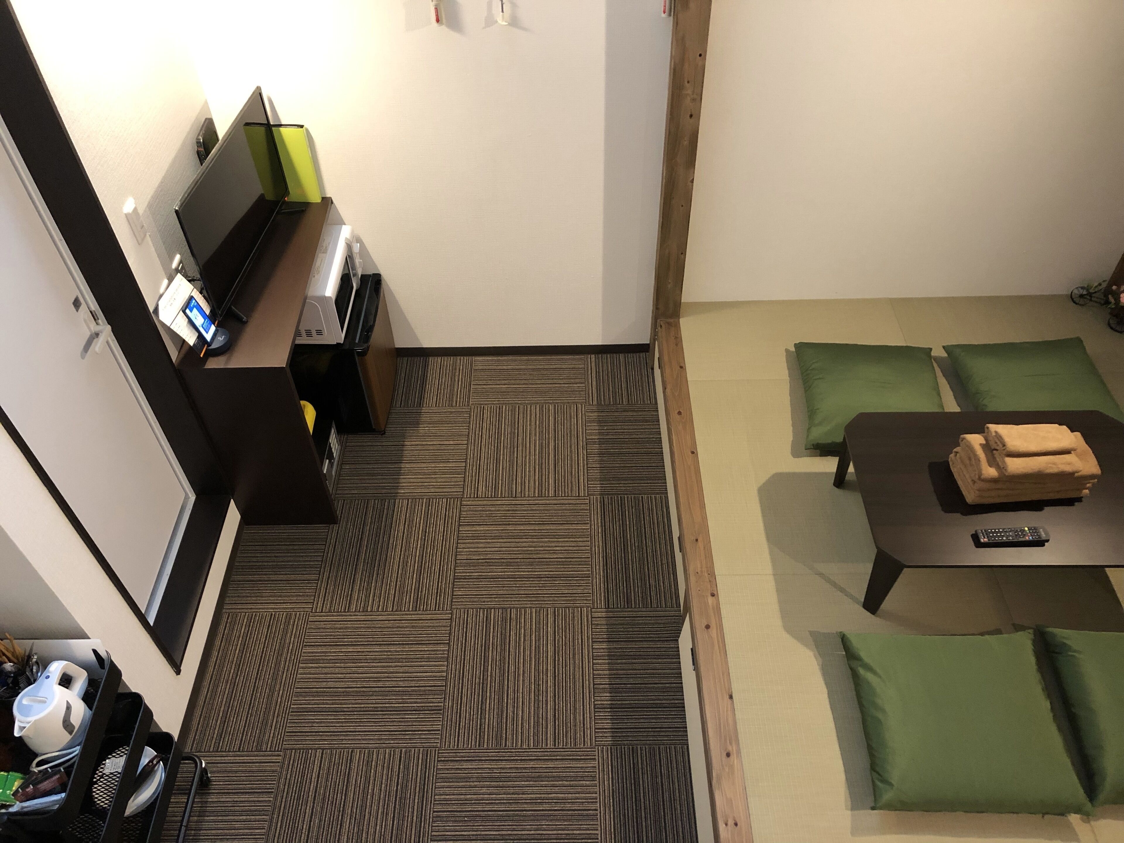 Habitación de hotel con un sofá, una mesita con un control remoto, una impresora y una lámpara verde.