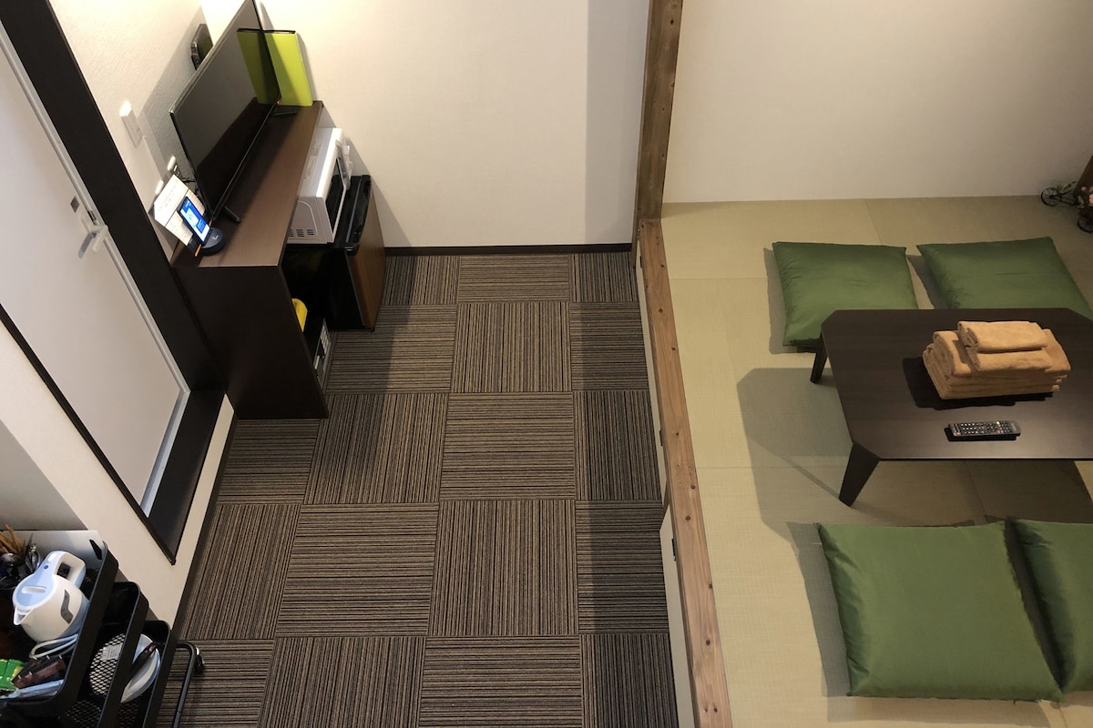 A hotel room with a sofa set, a small table with a remote control, a printer, and a green lamp.