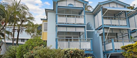 A multi-story building with balconies, surrounded by lush greenery.