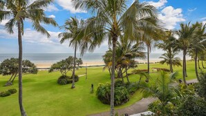 A tropical landscape with palm trees, a grassy area, and a view of the beach and ocean. - Villa at Tangalooma - Villa 14 (Moreton Island)