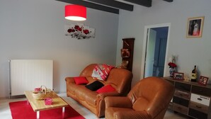 Ein Wohnzimmer mit einer braunen Ledersofa, einem Holztisch, einem roten Teppich, einer roten Pendelleuchte und einer Wand mit einem gerahmten Bild und einer Vase.