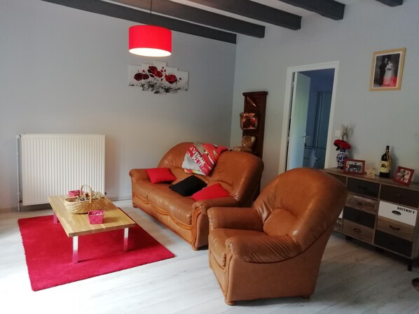 A living room with a brown leather sofa, a wooden coffee table, a red rug, a red pendant light, and a wall with a framed picture and a vase. - Country house Marmanhac (CANTAL) (Marmanhac)
