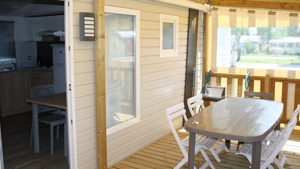 Een overdekte eethoek met een tafel en stoelen, een houten terras en uitzicht op een woonwijk.