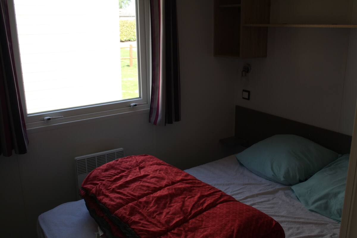 Een kleine, zwak verlichte kamer met een enkel bed, een raam met gordijnen en een radiator.