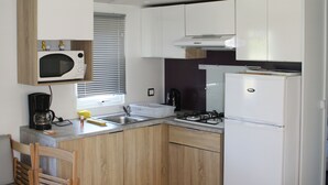 Een kleine keuken met een magnetron, fornuis, spoelbak en houten keukenkastjes.