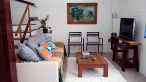 A living room with a sofa, two chairs, a coffee table, a TV, and a painting on the wall. - House - Mar Condominium Azul (Porto de Galinhas)