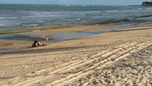 A sandy beach with footprints and a person sitting on the sand. - House - Mar Condominium Azul (Porto de Galinhas)