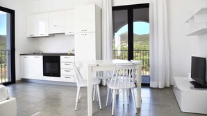 A modern kitchen with white cabinets, a built-in oven, and a dining area with a white table and chairs. -  Green Residence Olbia (Olbia)