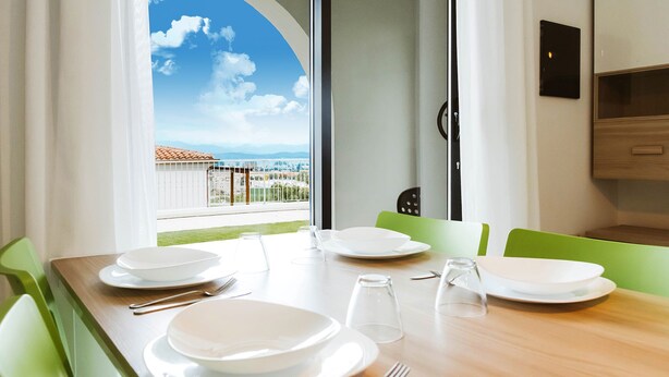 A dining area with a table set for four, a view of the sky and mountains, and a balcony with a railing. -  Green Residence Olbia (Olbia)