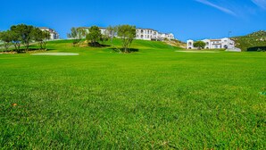 A large grassy field with a white building with multiple windows and a sloped roof. -  Green Residence Olbia (Olbia)