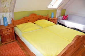 Un dormitorio con cama de madera, ropa de cama amarilla, una mesita de noche con un florero y una ventana con vista al cielo.