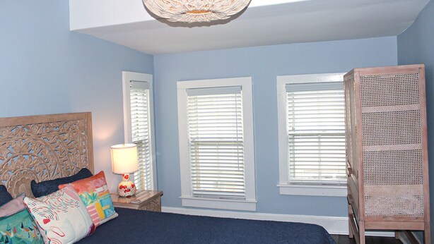 A bedroom with a bed, a nightstand, a lamp, and three windows with blinds. - Stylish Ocean Grove Apt - 4 Blocks from Beach & 2 Blocks from Downtown Asbury (Ocean Grove)