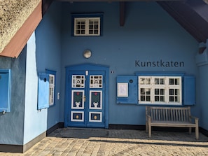 Un bâtiment à la façade bleue, avec un banc en bois et une porte ornée de panneaux de verre décoratifs.